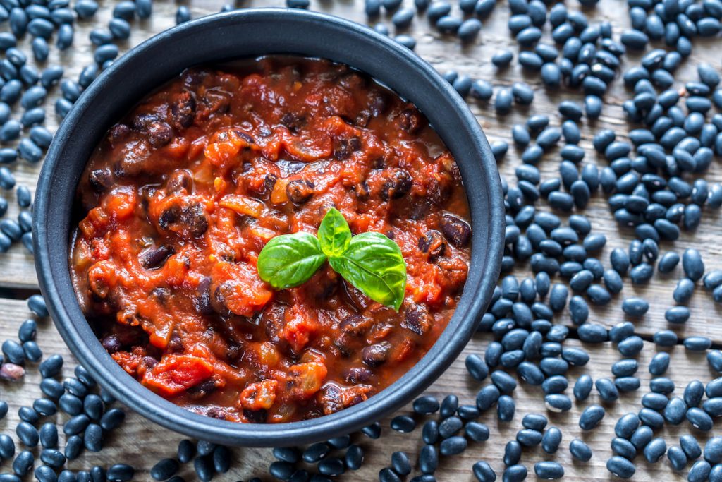 Bowl of black bean chili with raw black beans on background 