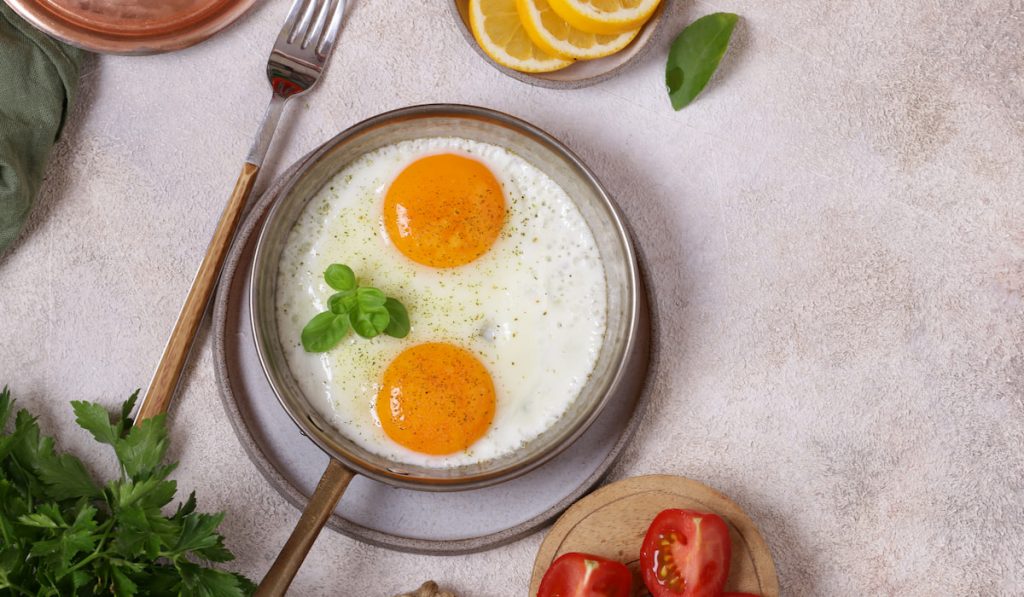 Fried eggs on frying pan with leaves, tomatoes, and lemon 