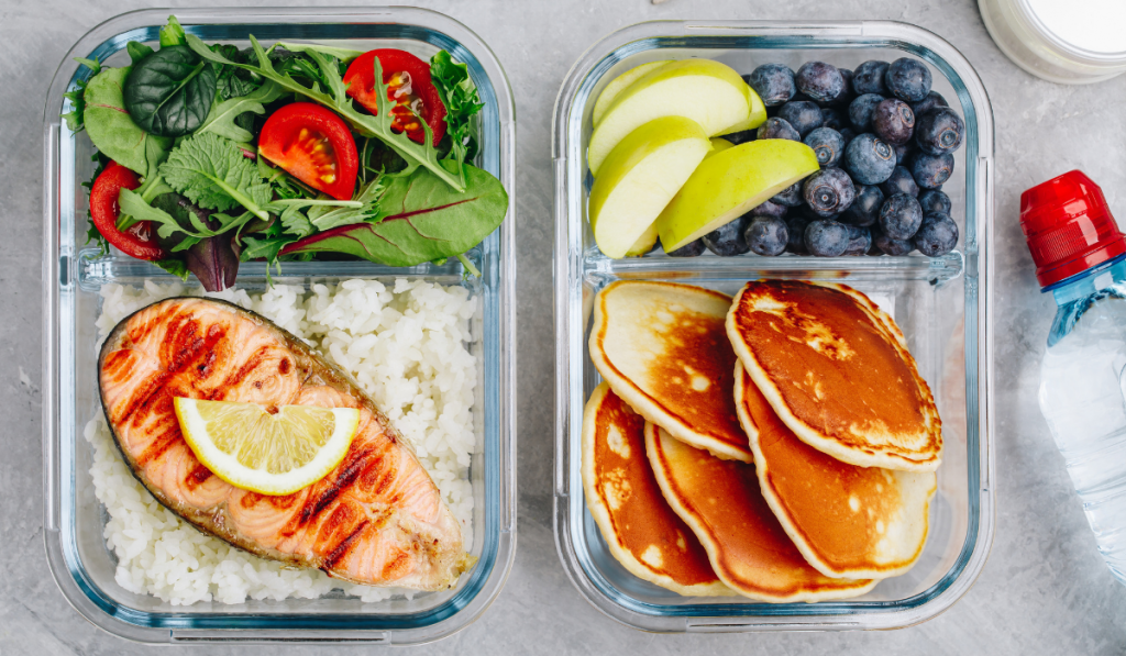 Meal prep containers with salmon, rice, green salad and pancakes, apple, blueberry.
