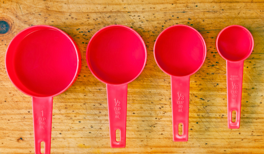Red measuring cups in different sizes on a timber board