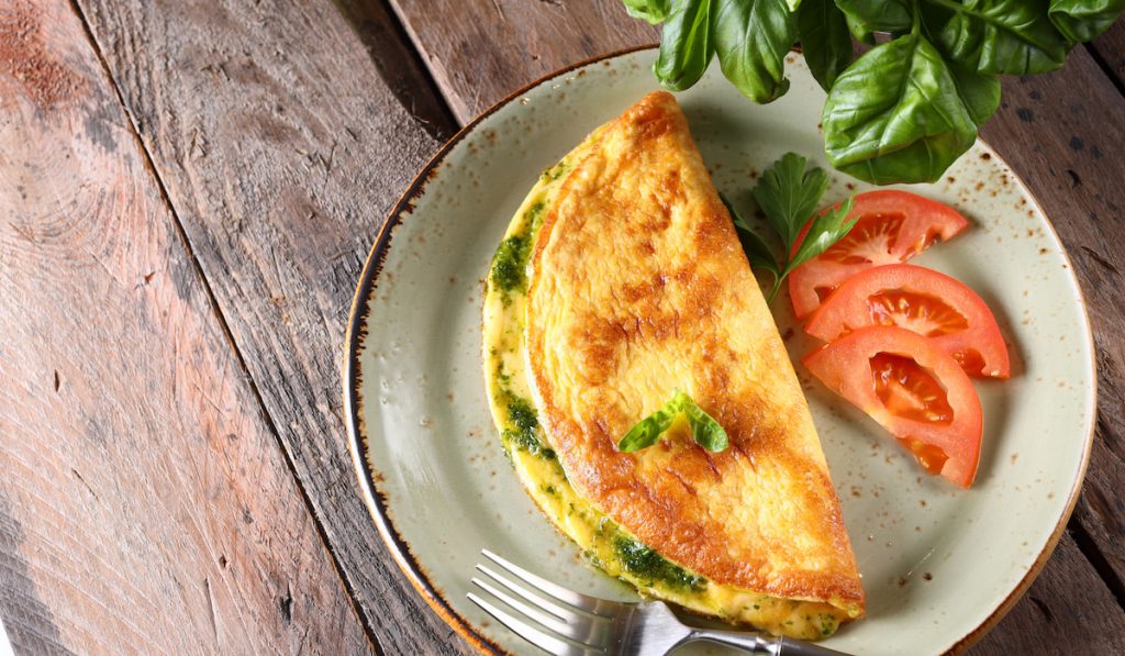 fried egg with herbs, tomatoes and fork on plate  wooden table 