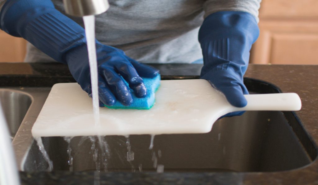 man wearing gloves washing white chopping board after preparing raw chicken 