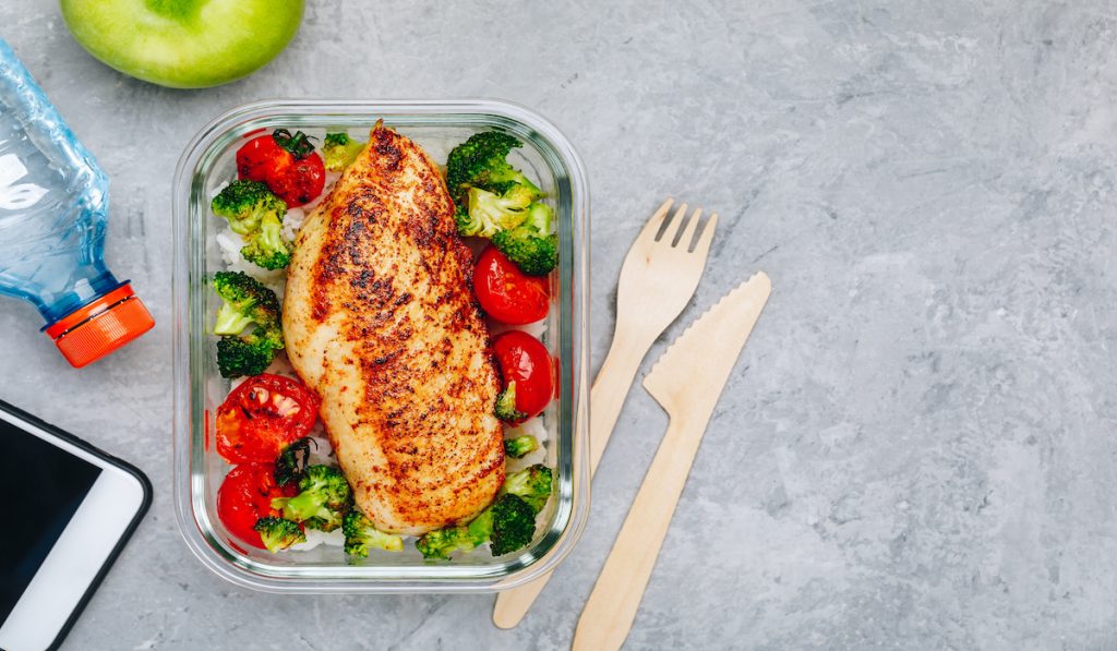 meal prep grilled chicken with rice, tomatoes and brocolli in a glass container 