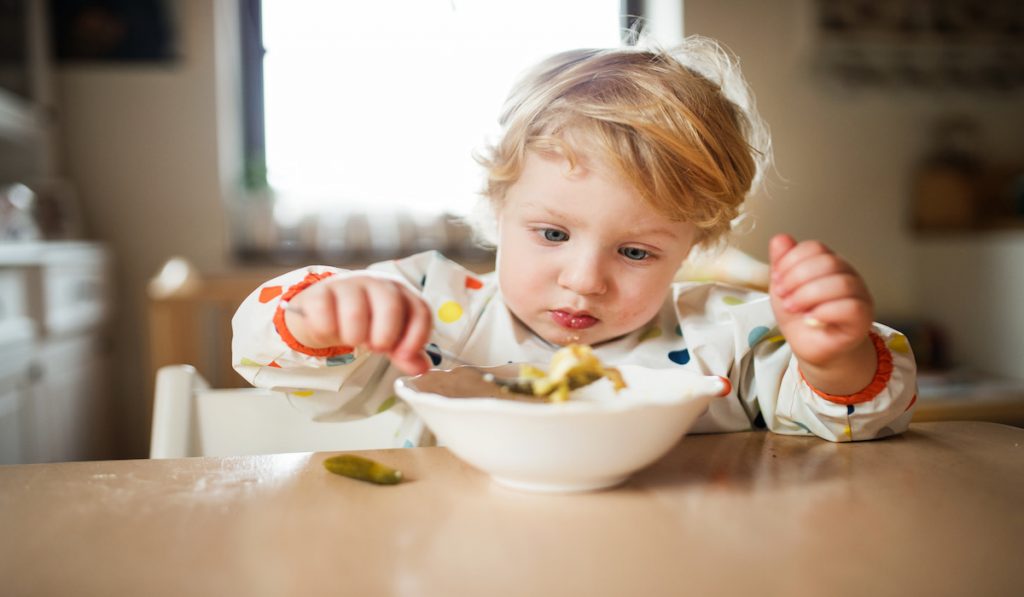 toddler boy eating some pasta alone 