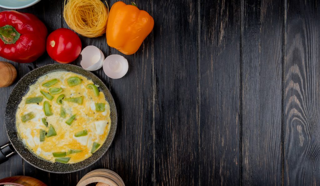 top view of fried egg on a frying pan with egg shells with colorful bell peppers