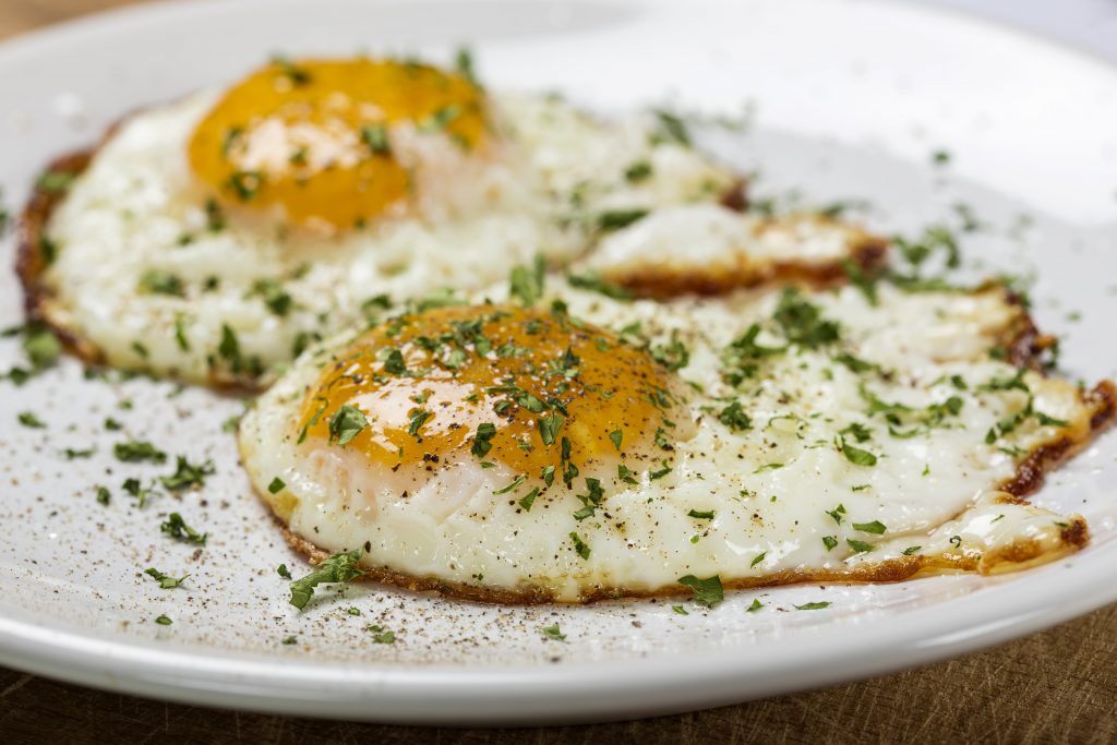 two fried eggs with herbs on top on white plate 