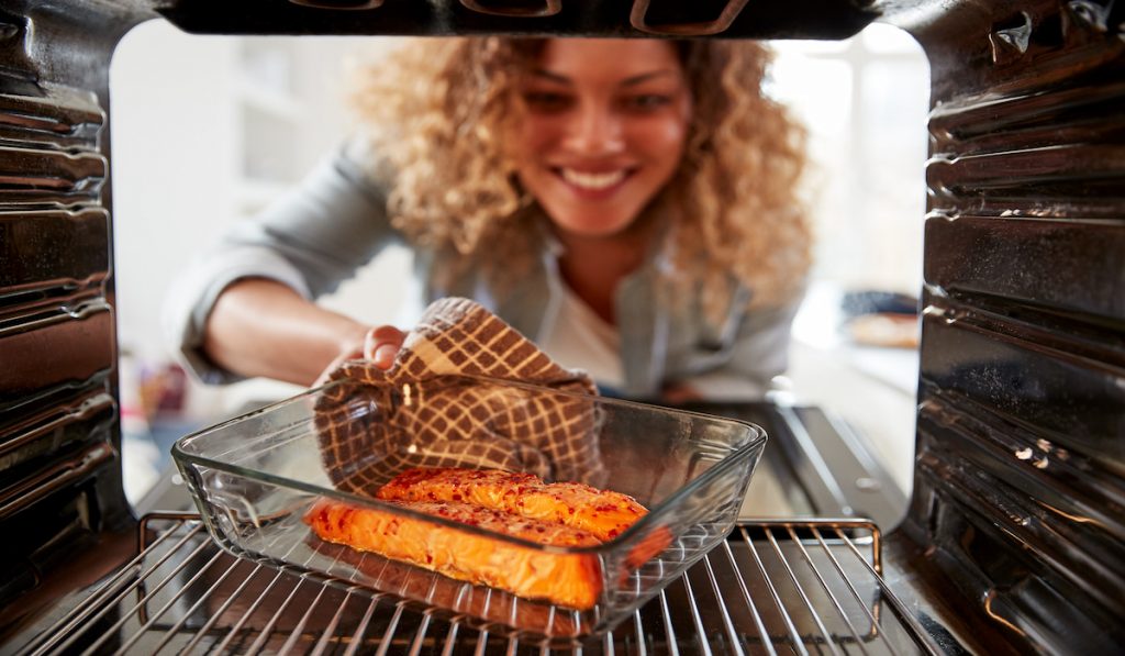woman checking baked salmon in the oven 