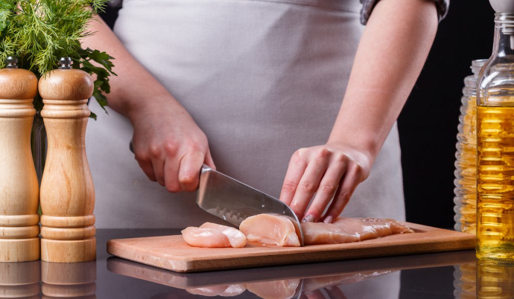 woman cutting and preparing chicken breast for meal prep