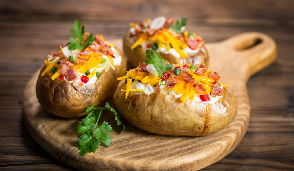 baked potatoes with cheese and bacon toppings on wooden chopping board 
